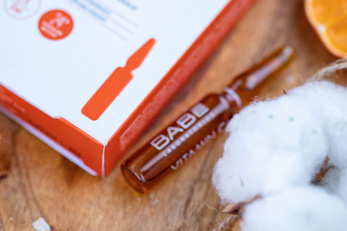 Braune Wirkstoffampulle aus Glas liegt neben ihrer Verpackung und getrockneten Orangenscheiben