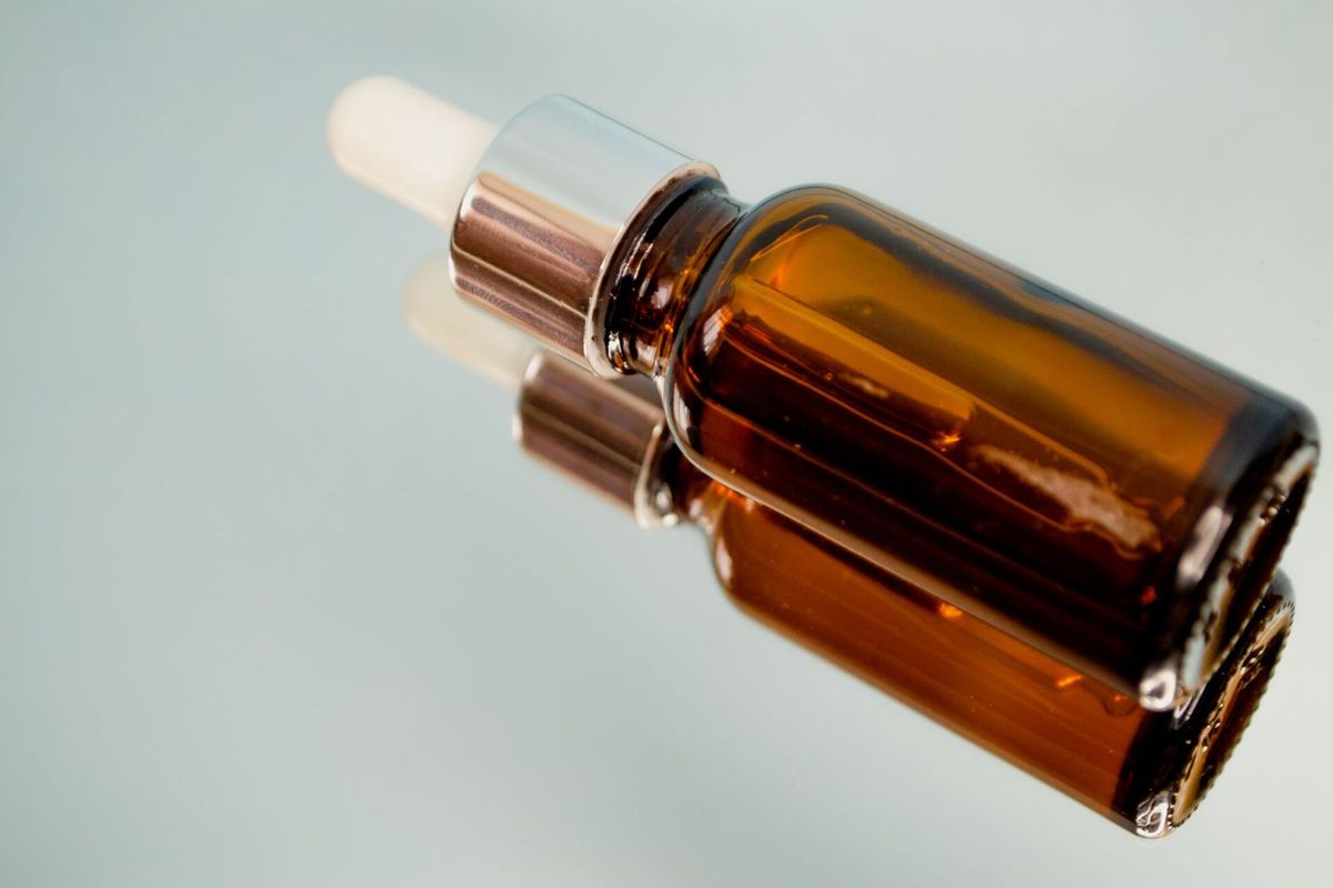 Braune Tropfflasche mit Pipette liegt auf einer spiegelnden hellen Fläche