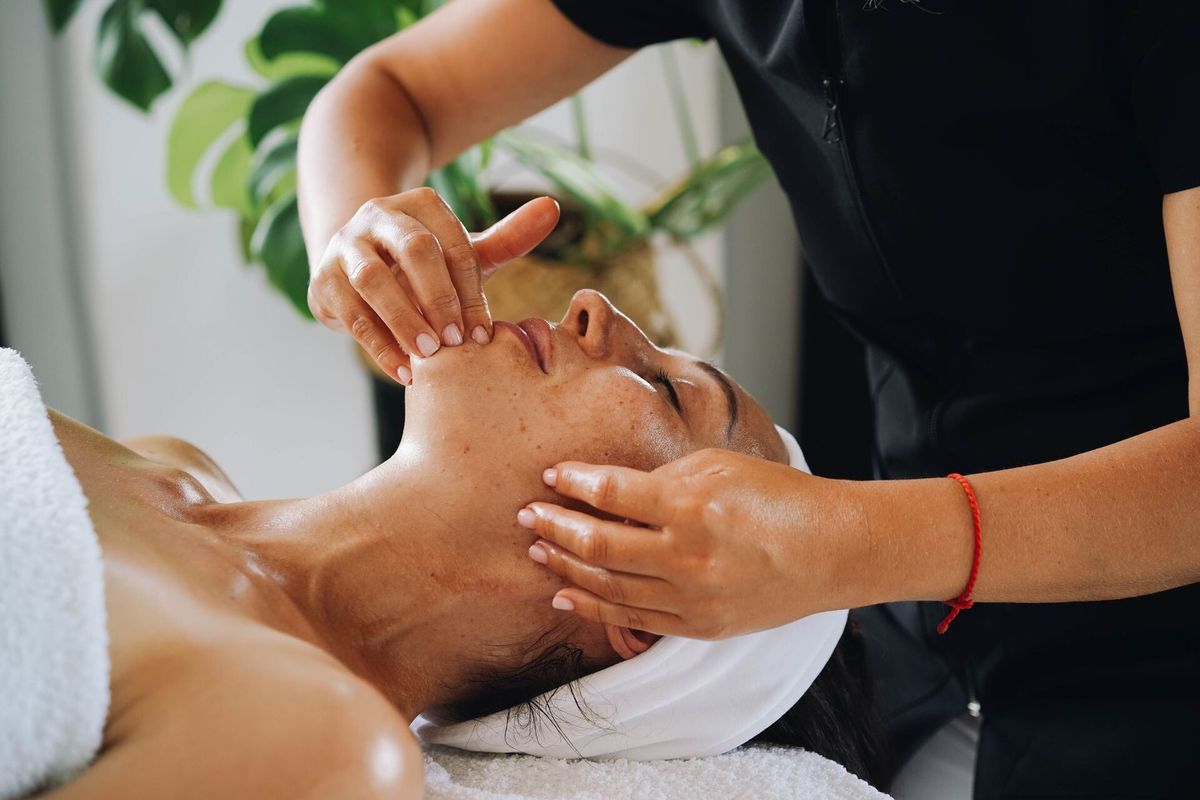 Sanfte Gesichtsmassage mit beiden Händen an Wange und Kinn einer entspannt liegenden Frau
