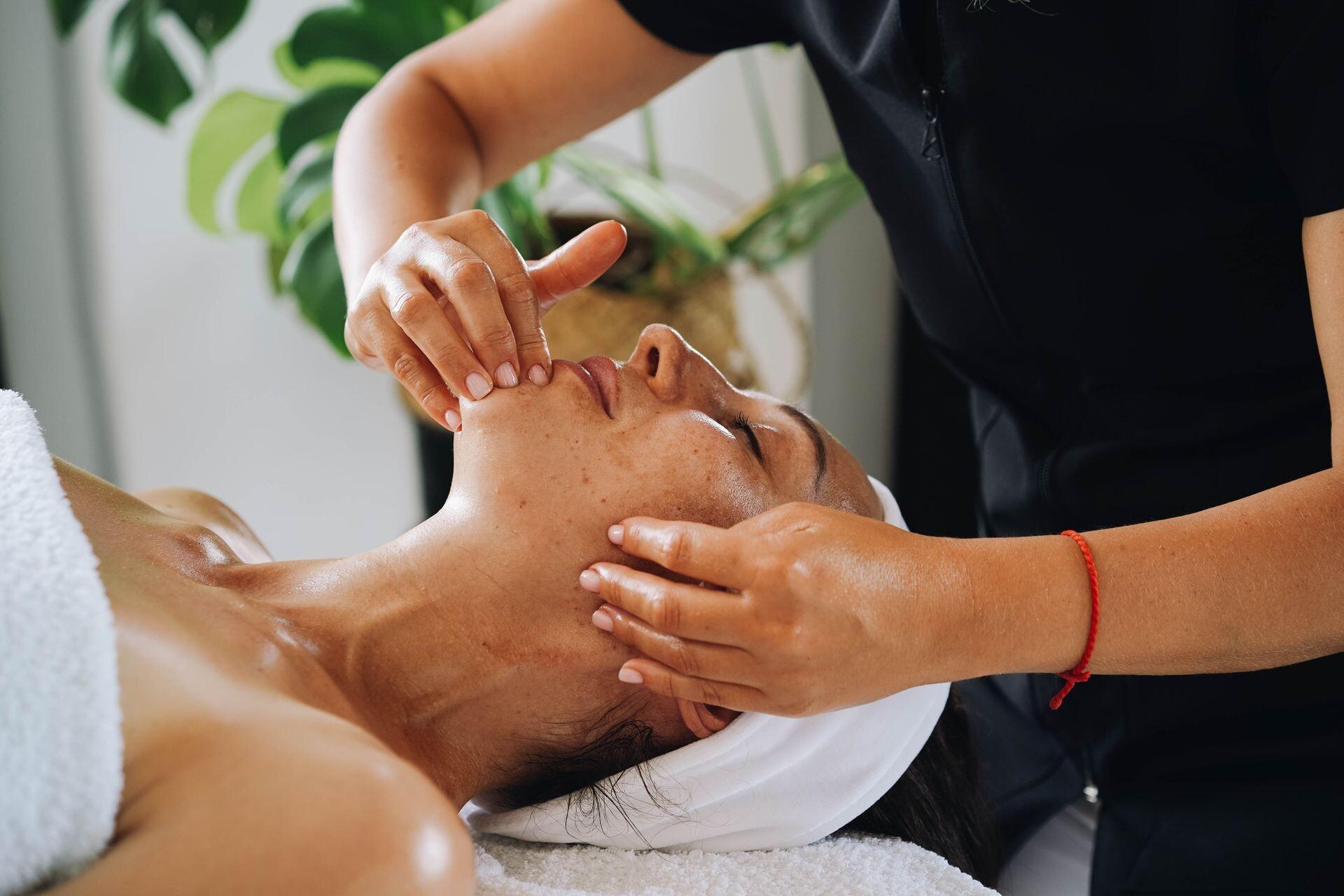 Sanfte Gesichtsmassage mit beiden Händen an Wange und Kinn einer entspannt liegenden Frau