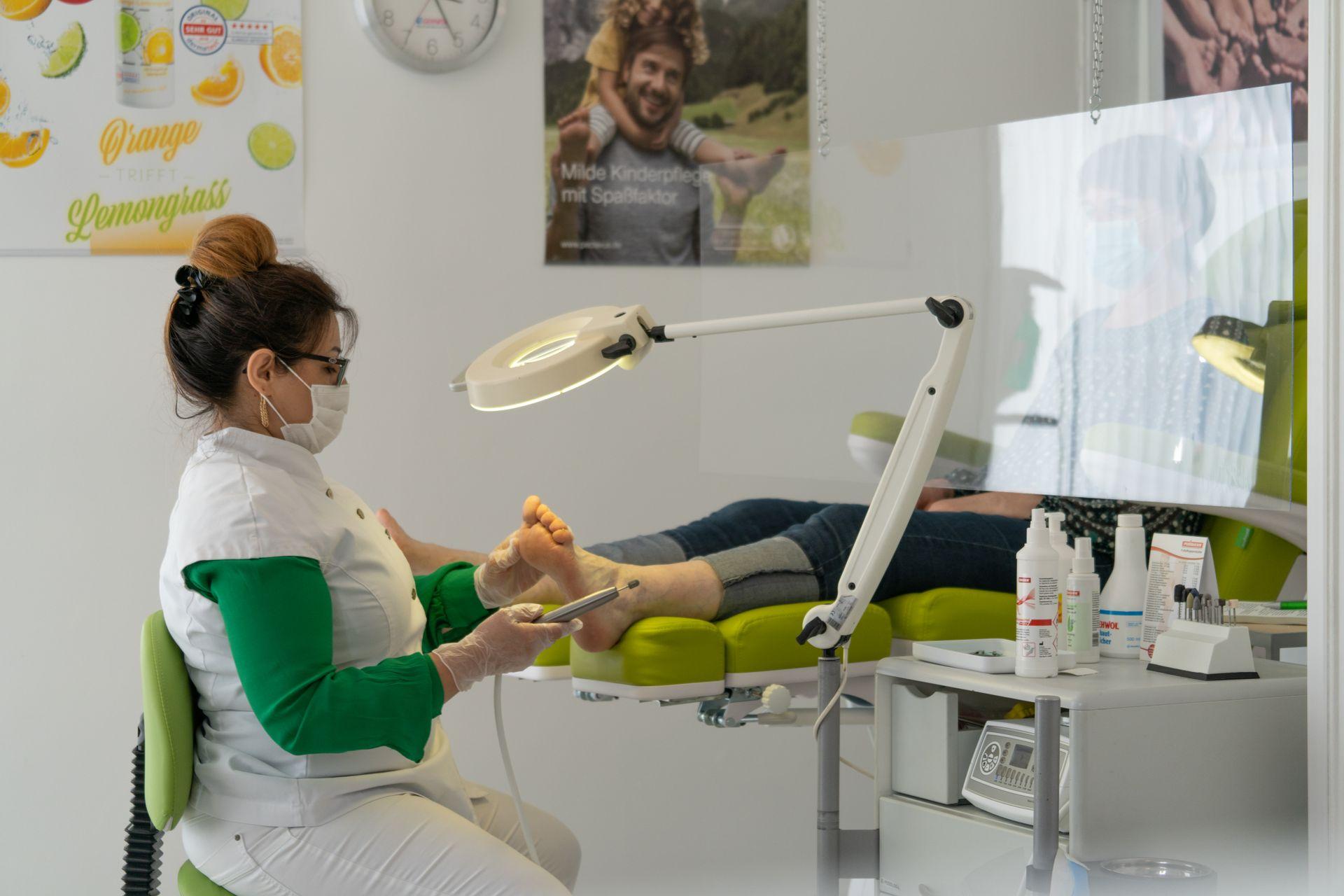 Fußpflegerin bearbeitet einen Fuß mit dem Fräser unter der Lupenlampe