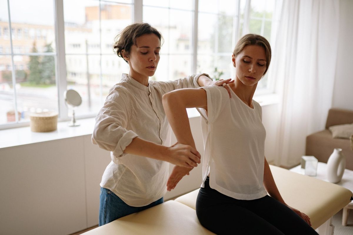 Therapeutin dehnt behutsam den Arm einer sitzenden Patientin in einem hellen Behandlungsraum