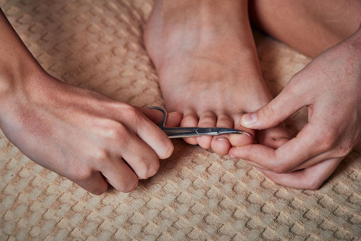 Nahaufnahme: Zwei Hände kürzen mit einer Nagelschere behutsam einen Zehennagel