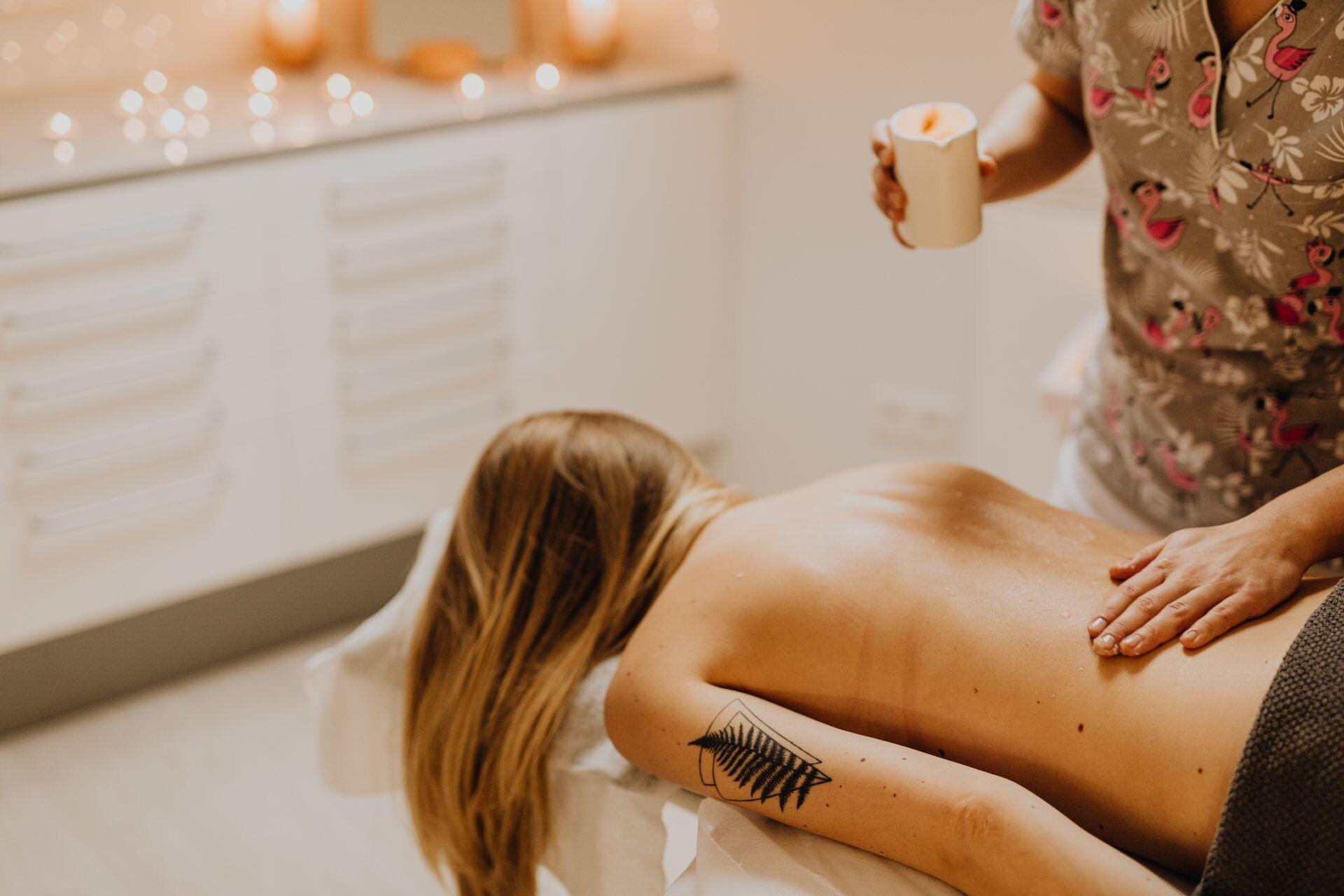 Rückenmassage mit warmem Öl bei Kerzenschein, die Therapeutin hält eine Massagekerze