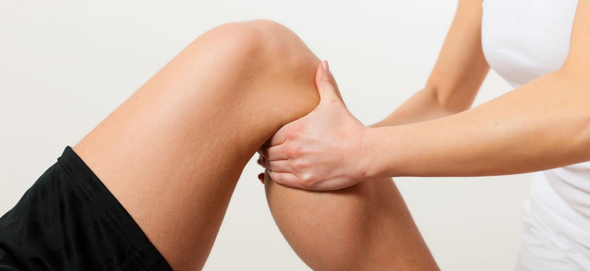 Physiotherapeutin behandelt mit ihren Händen das Knie einer Patientin